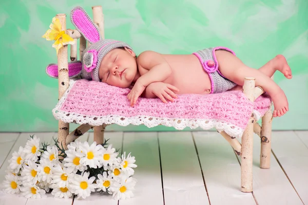 Newborn baby girl in a knitted hare costume sleeping on a wooden crib birch