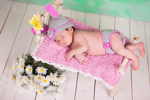 Newborn baby girl in a knitted hare costume sleeping on a wooden crib birch