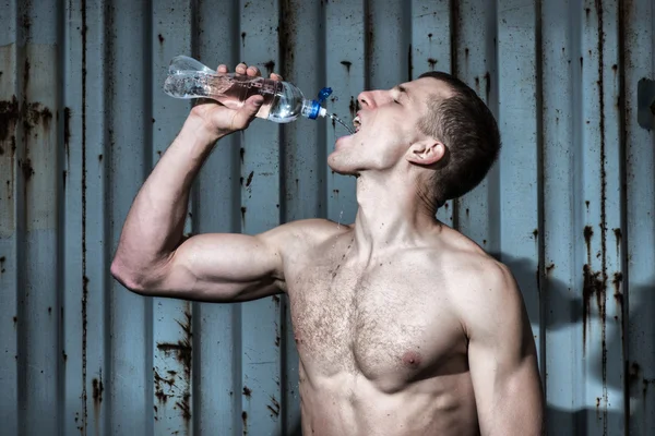 Muscular young man drinks water after sport exercise