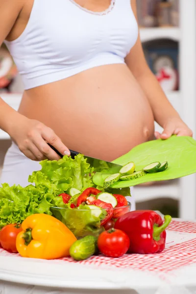 Close-up. Pregnant woman in the kitchen cuts different vegetables on spring salad.