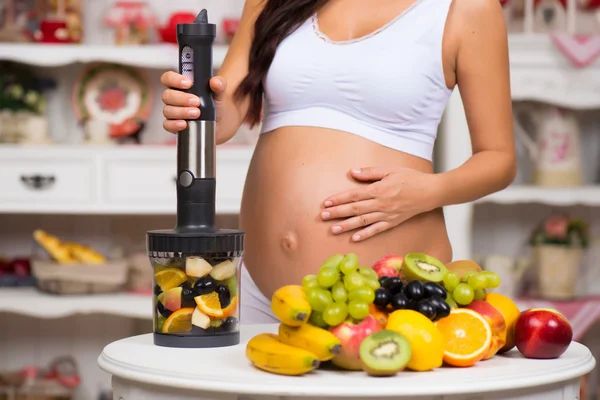 Belly of a pregnant woman, blender, mixer and fresh fruit closeup