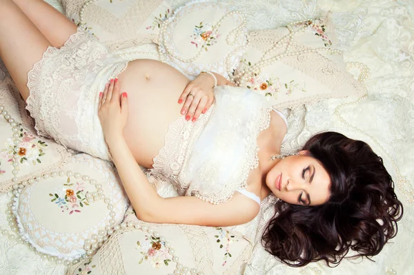 Pregnant brunette woman in a lace dress on the bed, top view