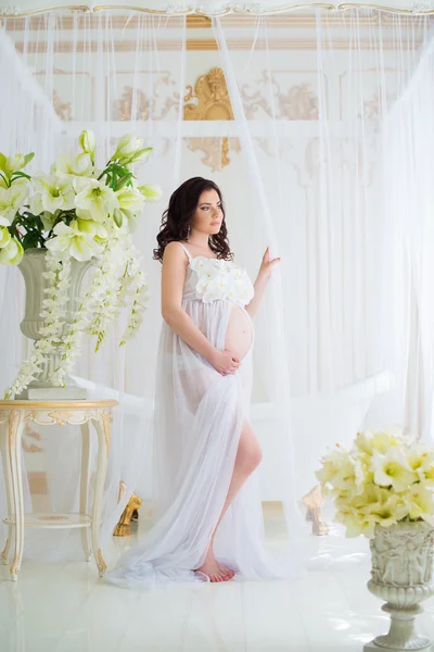 Beautiful pregnant girl in interior with flowers and tulle curtains
