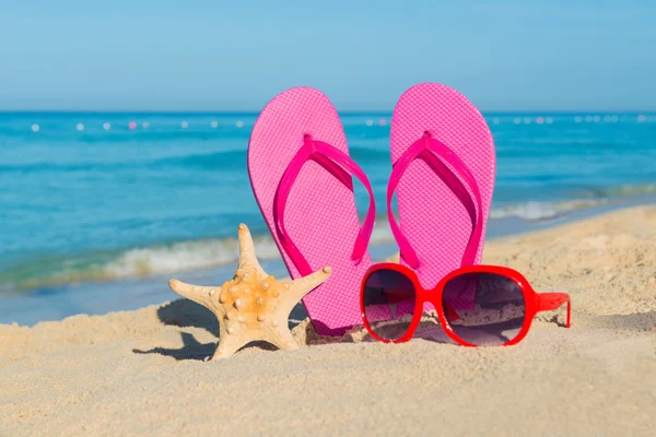 The sea, beach, sand and women\'s accessories: pink flip-flops, red sunglasses and starfish
