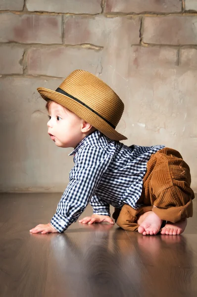 Llittle boy in retro hat and corduroy trousers learning to crawl on floor on all fours