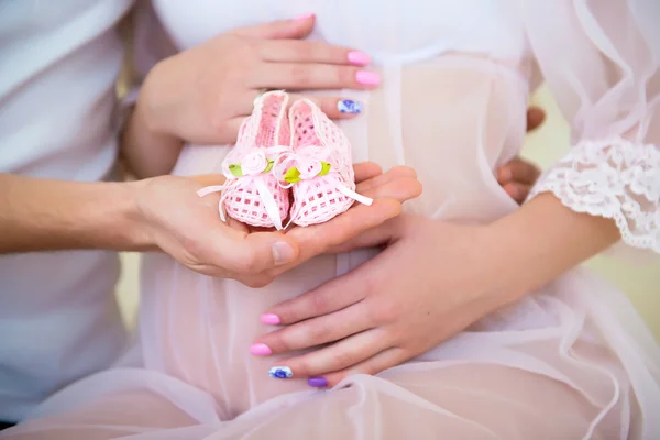 Baby booties for the newborn daughter on a background of a pregnant belly