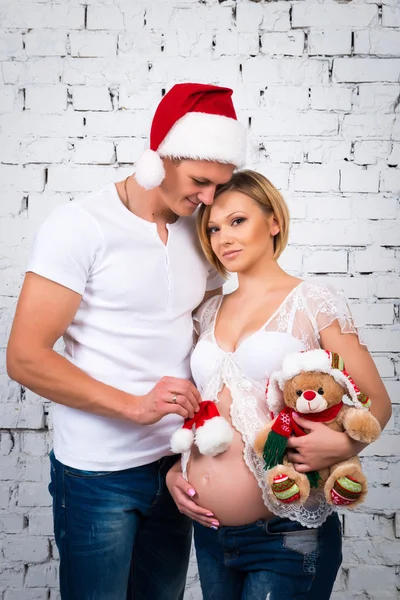 Young pregnant family with a New Year Santa hat and Christmas teddy bear. Happy pregnancy