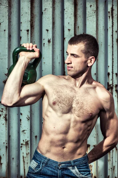 Young athlete man doing workout with heavy weights on the background of a gray metal wall