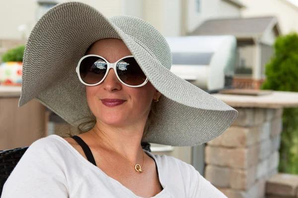 Woman in Hat and Sunglasses Sitting on Back Patio