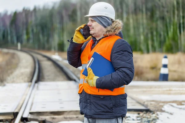 Railroad worker with documentation and smartp hone on railway crossing