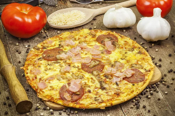 Pizza wit bacon and salami near tomatoes and garlic on wooden table