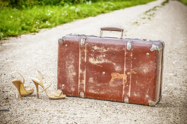 Old suitcase and high heel sandals on the rural road