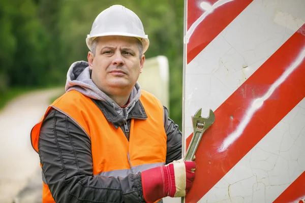 Worker with adjustable wrench on the bridge repairing road sign