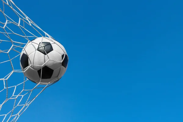 Soccer ball in goal net with blue sky