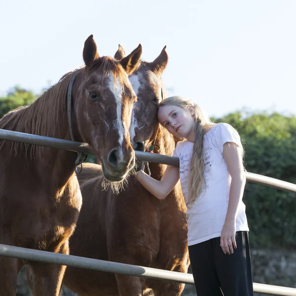 Young blond girl poses with two brown horses