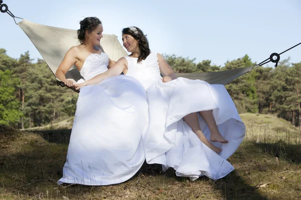 Two brides in hammock against blue sky with forest background