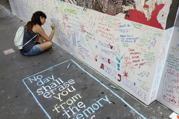 Young woman sits on pavement near ground zero and writes on wall