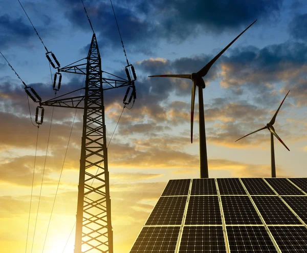 Solar panels with wind turbines and electricity pylon at sunset.