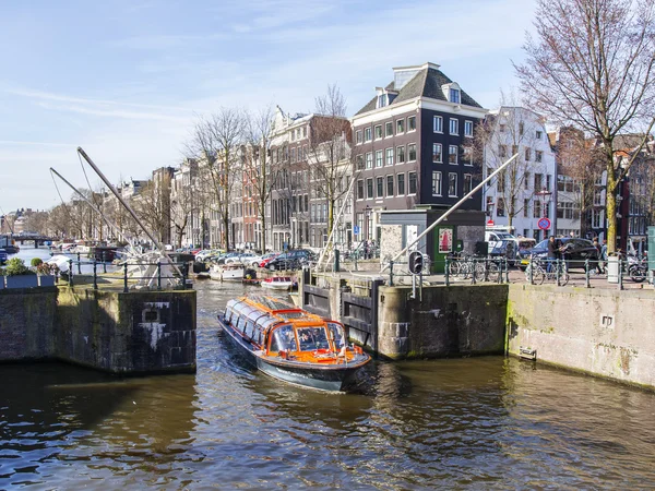 AMSTERDAM, NETHERLANDS on APRIL 1, 2016. Typical urban view in the spring morning. The channel and buildings of the XVII-XVIII construction on embankments. The walking ship floats on the channel