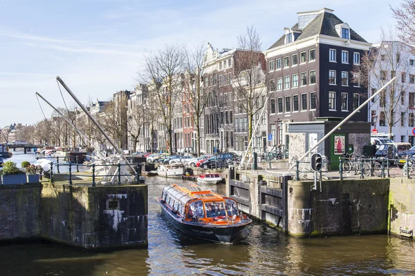 AMSTERDAM, NETHERLANDS on APRIL 1, 2016. Typical urban view in the spring morning. The channel and buildings of the XVII-XVIII construction on embankments. The walking ship floats on the channel
