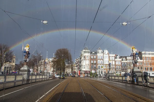 AMSTERDAM, NETHERLANDS on MARCH 27, 2016. A view of the city in the spring afternoon during a rain through a wet window of the tram. A rainbow in the sky in the distance