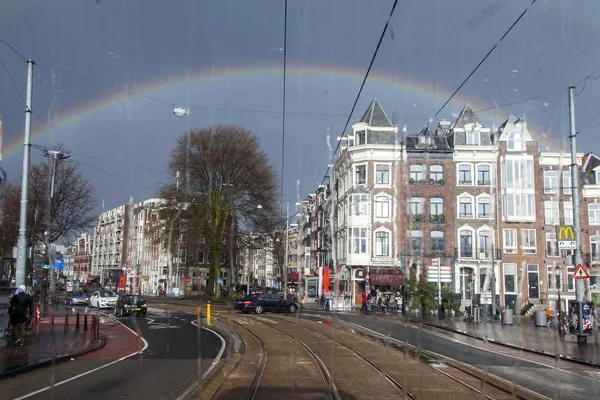 AMSTERDAM, NETHERLANDS on MARCH 27, 2016. A view of the city in the spring afternoon during a rain through a wet window of the tram. A rainbow in the sky in the distance