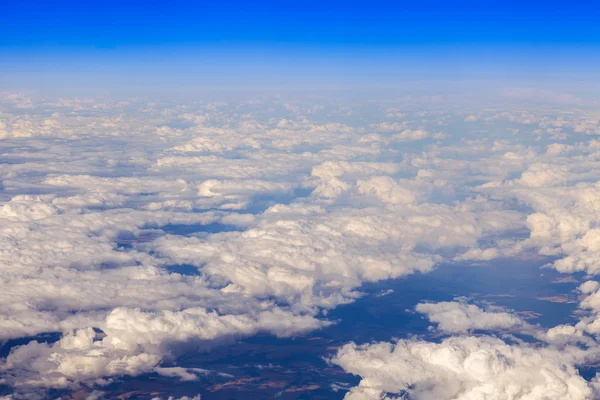 Heavenly landscape. A view of white clouds and the terrestrial surface lit with the sun from a window of the flying plane