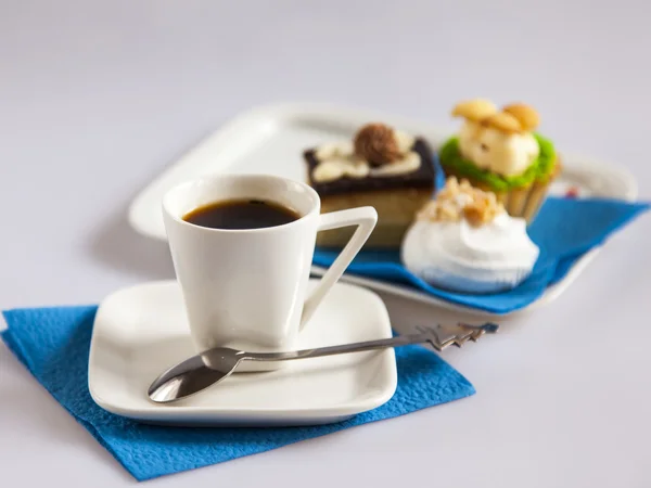 Cup with black coffee and a plate with cakes on a background