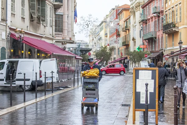 NICE, FRANCE - on JANUARY 11, 2016. A typical urban view in rainy weather. The worker pushes the cart with products down the street on the market