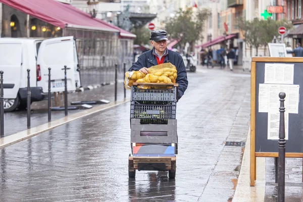 NICE, FRANCE - on JANUARY 11, 2016. A typical urban view in rainy weather. The worker pushes the cart with products down the street on the market