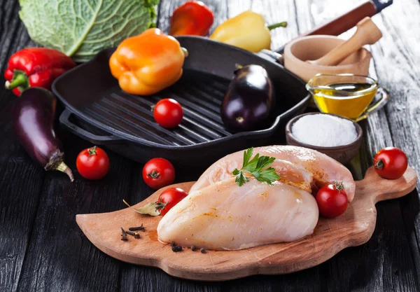 Raw chicken fillets on wooden cutting board, with vegetables