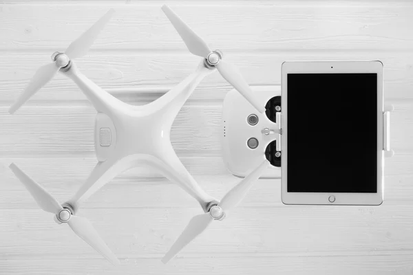 Quadrocopter, tablet and remote control on a white wooden background