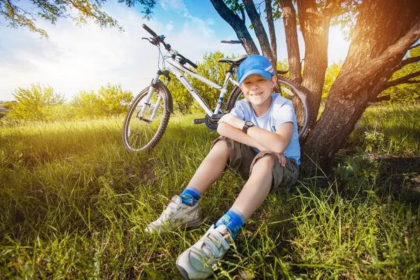 Happy kid with a bicycle resting under a tree