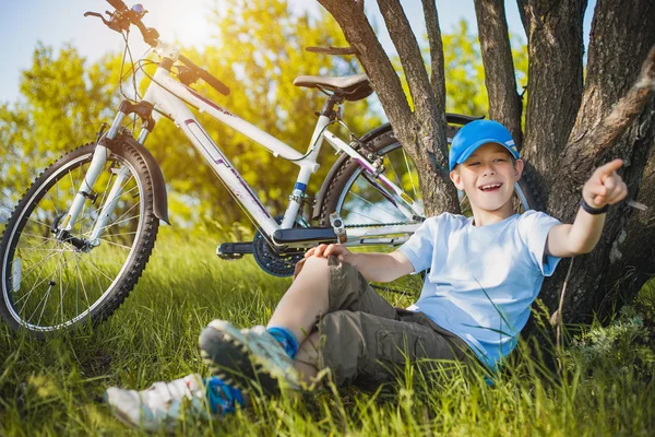 Happy kid with a bicycle resting under a tree