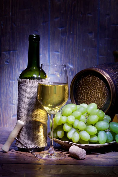 Cassa in legno con bottiglie di vino, botte, calici e uva su un ... Botte tavolo con vetro