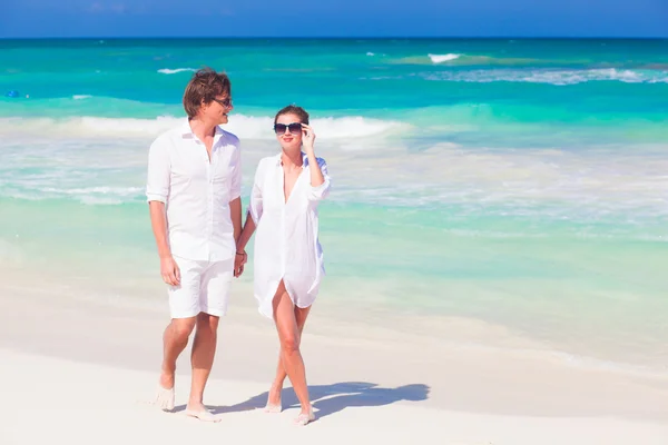 Portrait of happy young couple in sunglasses in white clothes walking on tropical beach