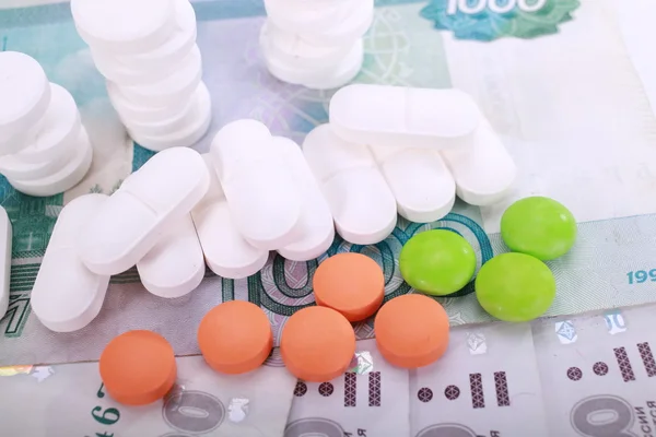 Pills of different colors on money background.