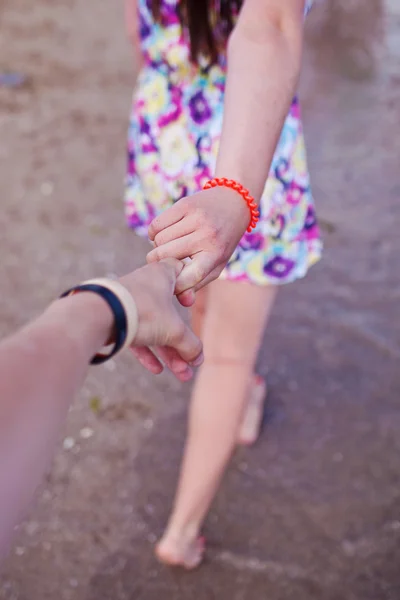 Young girl supporting man, holding hand on the beach