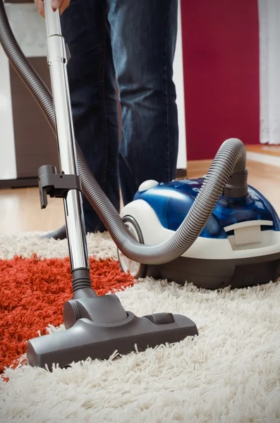 Man vacuums shaggy carpet in the apartment.