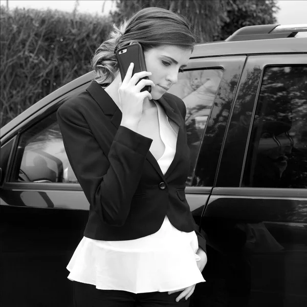 Beautiful young business woman in front of car making phone call