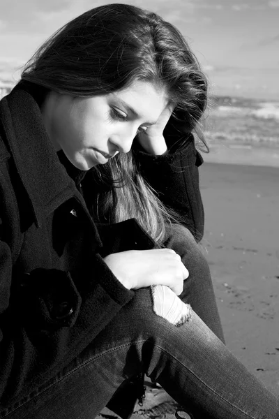 Sad female teenager sitting in front of ocean