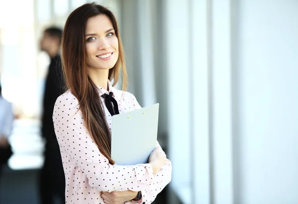 Business woman standing in foreground with a tablet in her hands, her co-workers discussing business matters in background