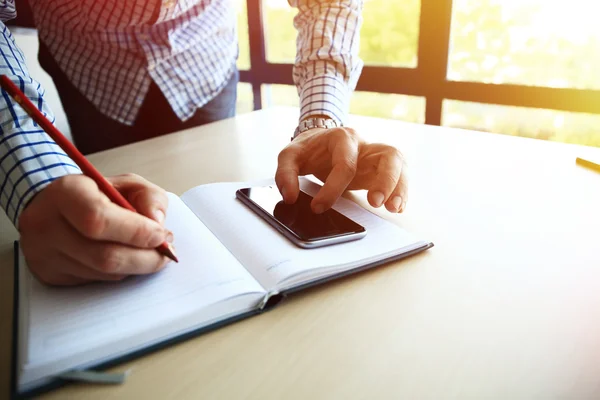 Male hand holding pencil ready to make note in opened notebook while looking at cellphone. Businessman or employee at workplace writing business ideas, plans at personal organizer