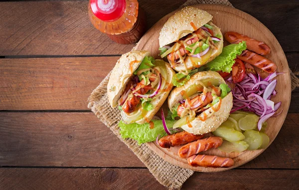 Hot dog - sandwich with pickles, red onions and lettuce on wooden background