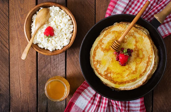 Golden pancakes with cranberry jam and honey in a rustic style
