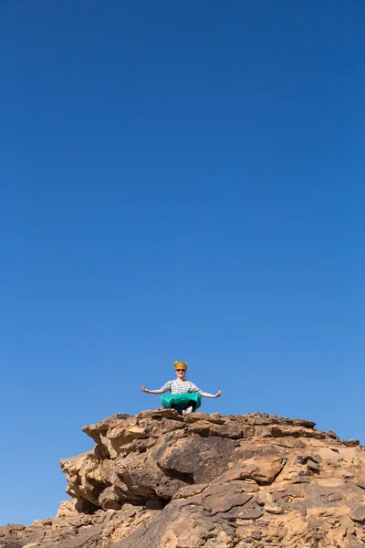 Tourist spreading arms on big rock in desert