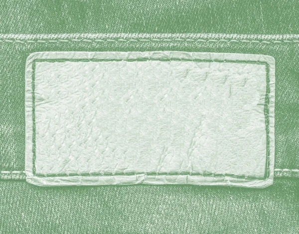 Pale green leather label on green jeans background