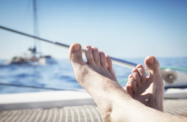 Man lounging on a catamaran sailboat trampoline with her feet propped up and crossed.