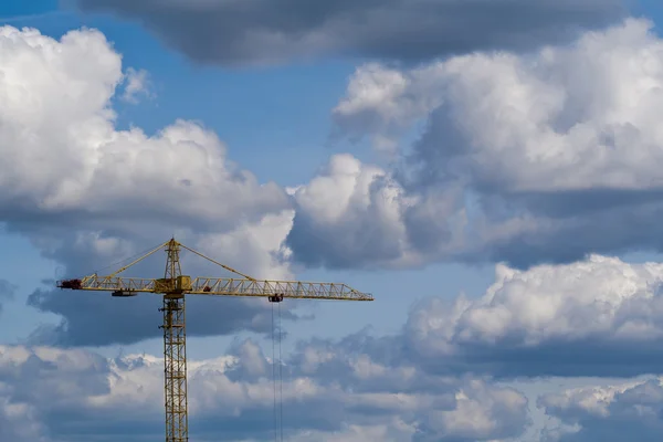 The building crane against the blue sky with picturesque clouds.