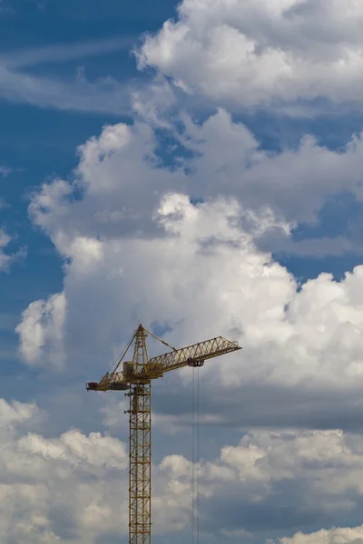 The building crane against the blue sky with picturesque clouds.